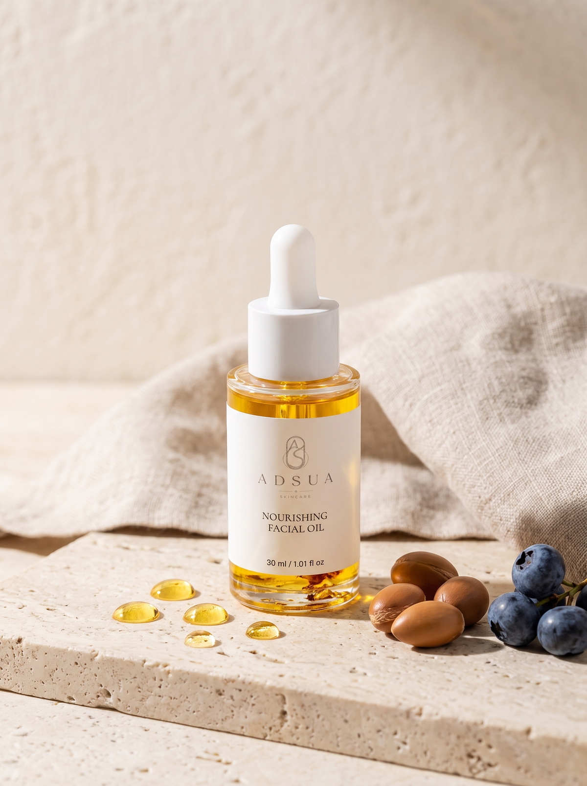 Adsua Nourishing Facial Oil op travertijn in ochtendlicht, met gouden oliedruppels, arganpitten en bosbessen