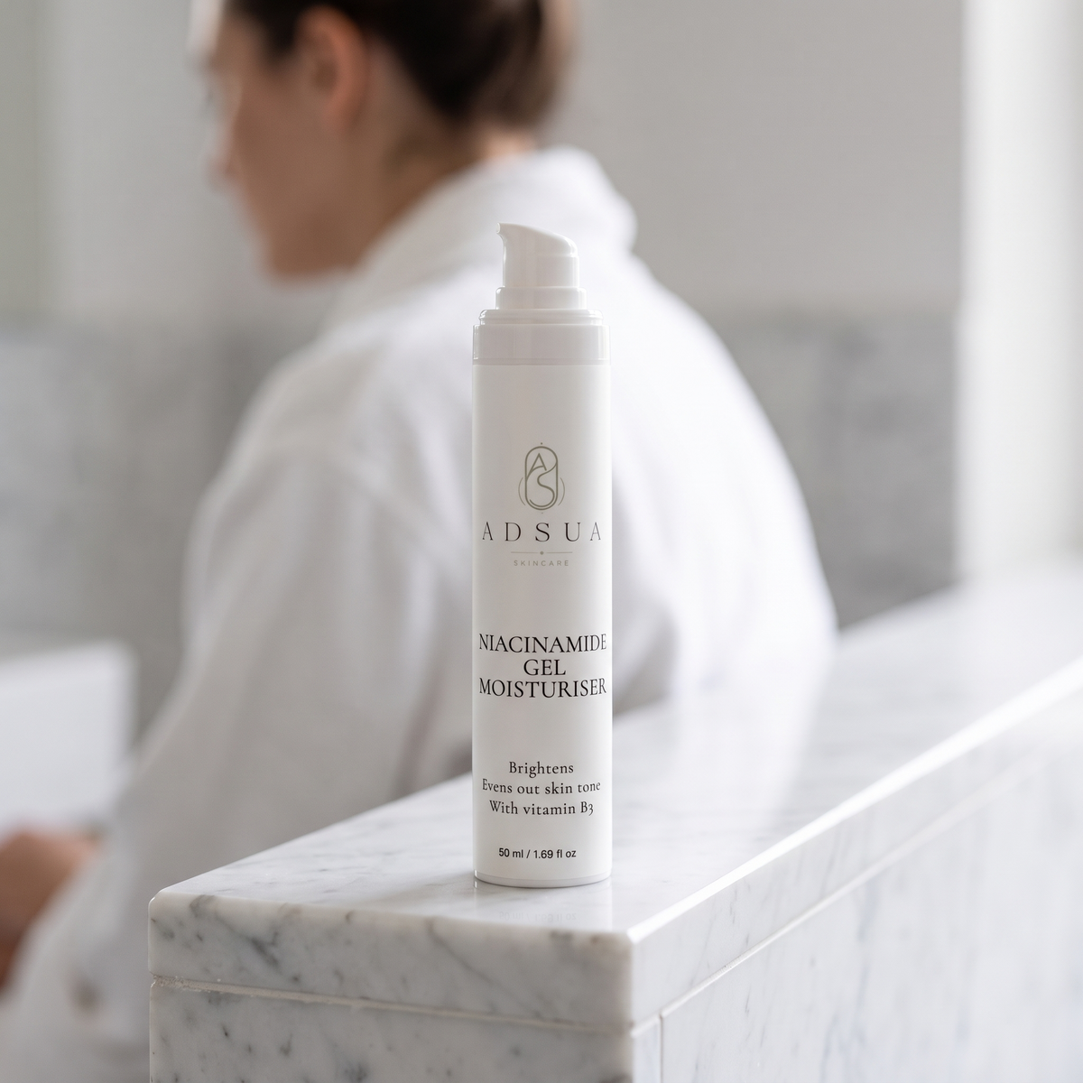 Adsua Niacinamide Gel Moisturiser op een marmeren badkamerrand, met een vrouw op de achtergrond