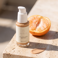 Adsua Sunscreen SPF30 with tint op travertijn in de zon, met een veeg van de getinte crème op de steen en een halve mandarijn