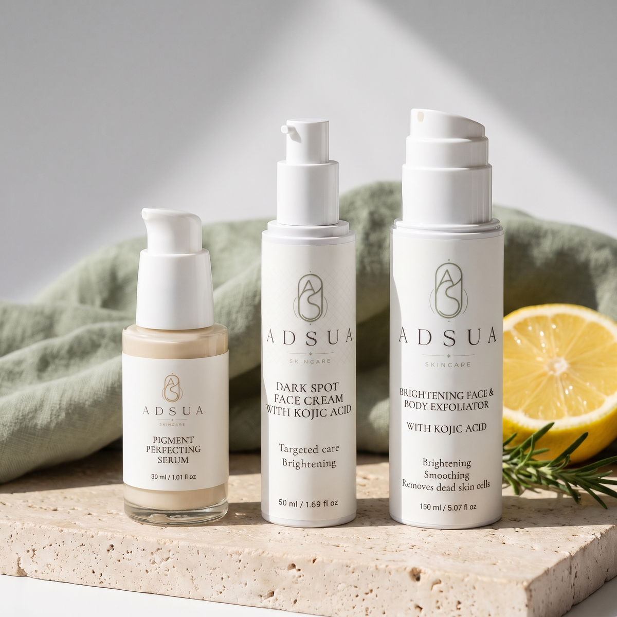 De Adsua dark spot routine naast elkaar op travertijn met saliegroen linnen: het Pigment Perfecting Serum, de Dark Spot Face Cream en de Brightening Face & Body Exfoliator